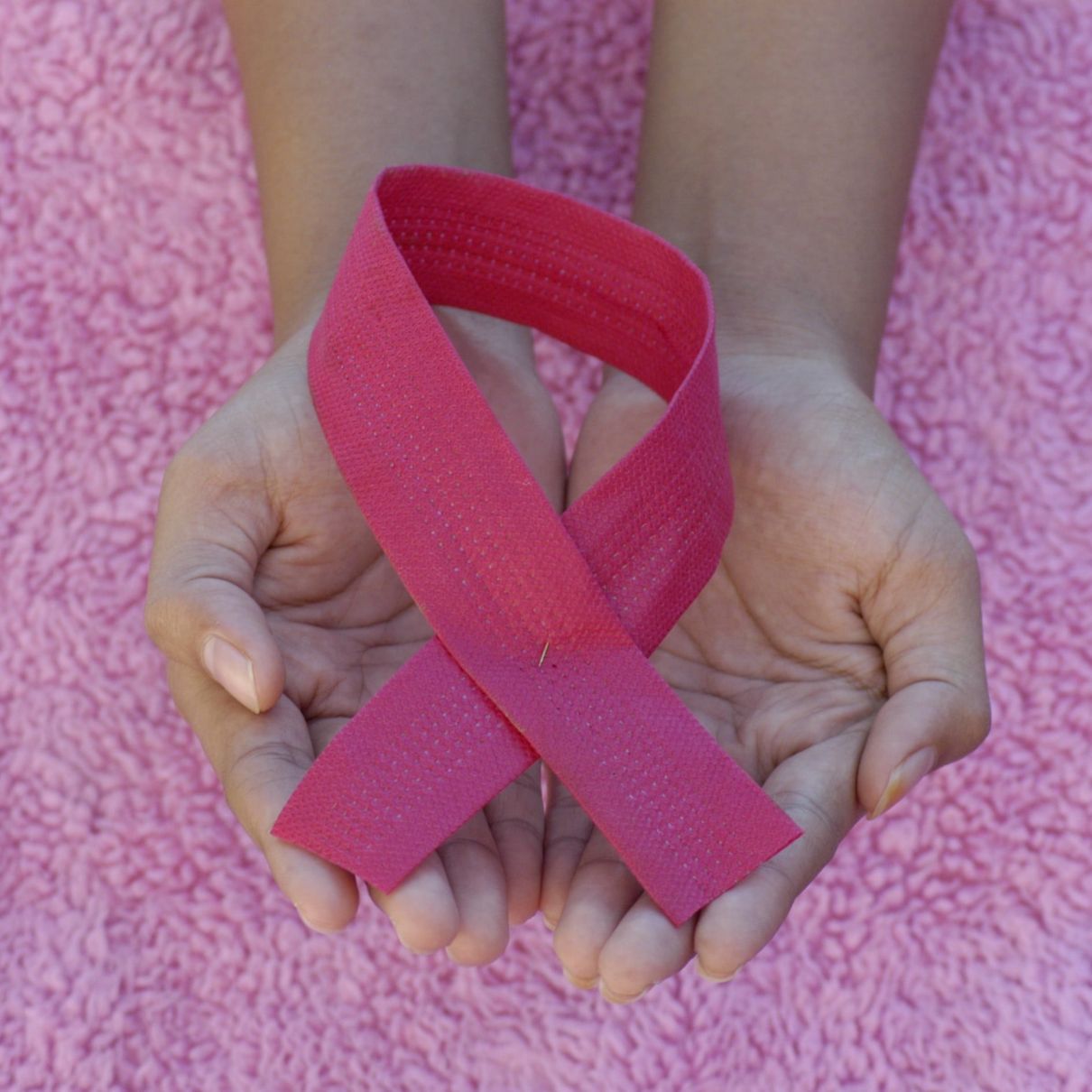 hands holding a a large pink ribbon against a pink fabric